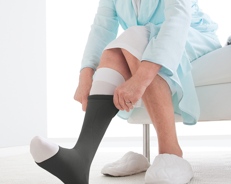 A seated elderly woman, pulling on a compression stocking over her leg. A seated elderly woman, pulling on a compression stocking over her leg.